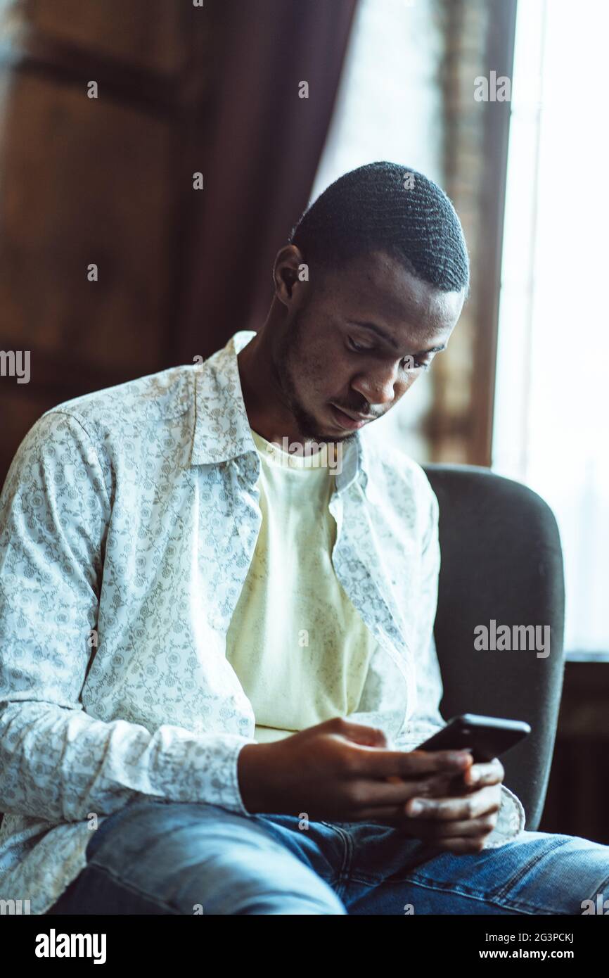 Junge Schwarze Kerl Chattet Im Telefon Sitzen Im Gemütlichen Büro Stockfoto