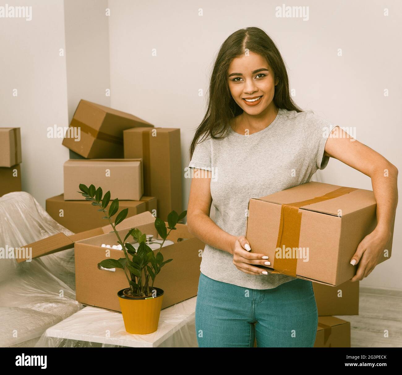 Schöne hispanische Frau mit Box in neuem Zuhause Stockfoto