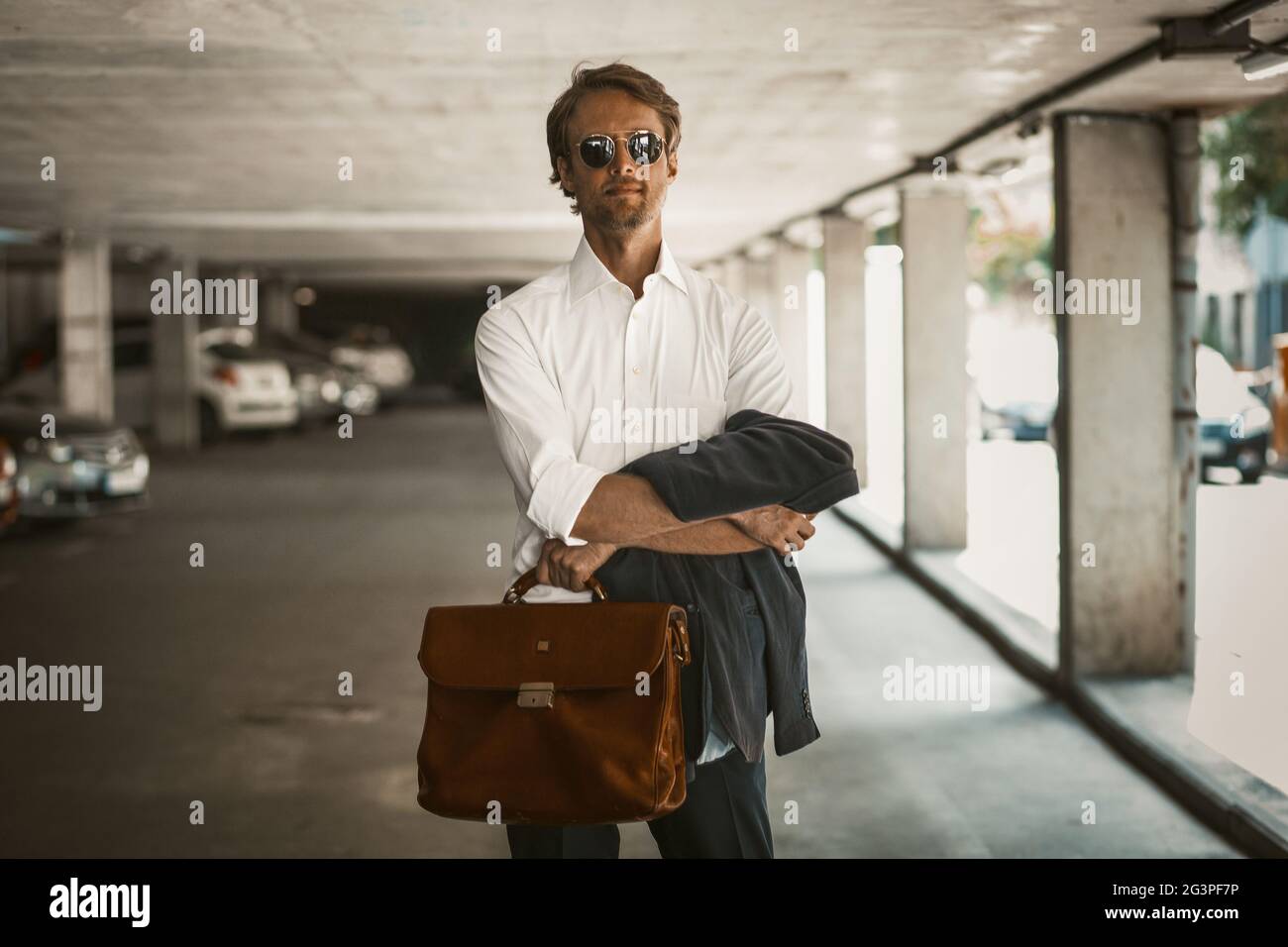 Charmanter Geschäftsmann, der auf einer Perking-Lot steht und seine Jacke und Aktentasche hält Stockfoto