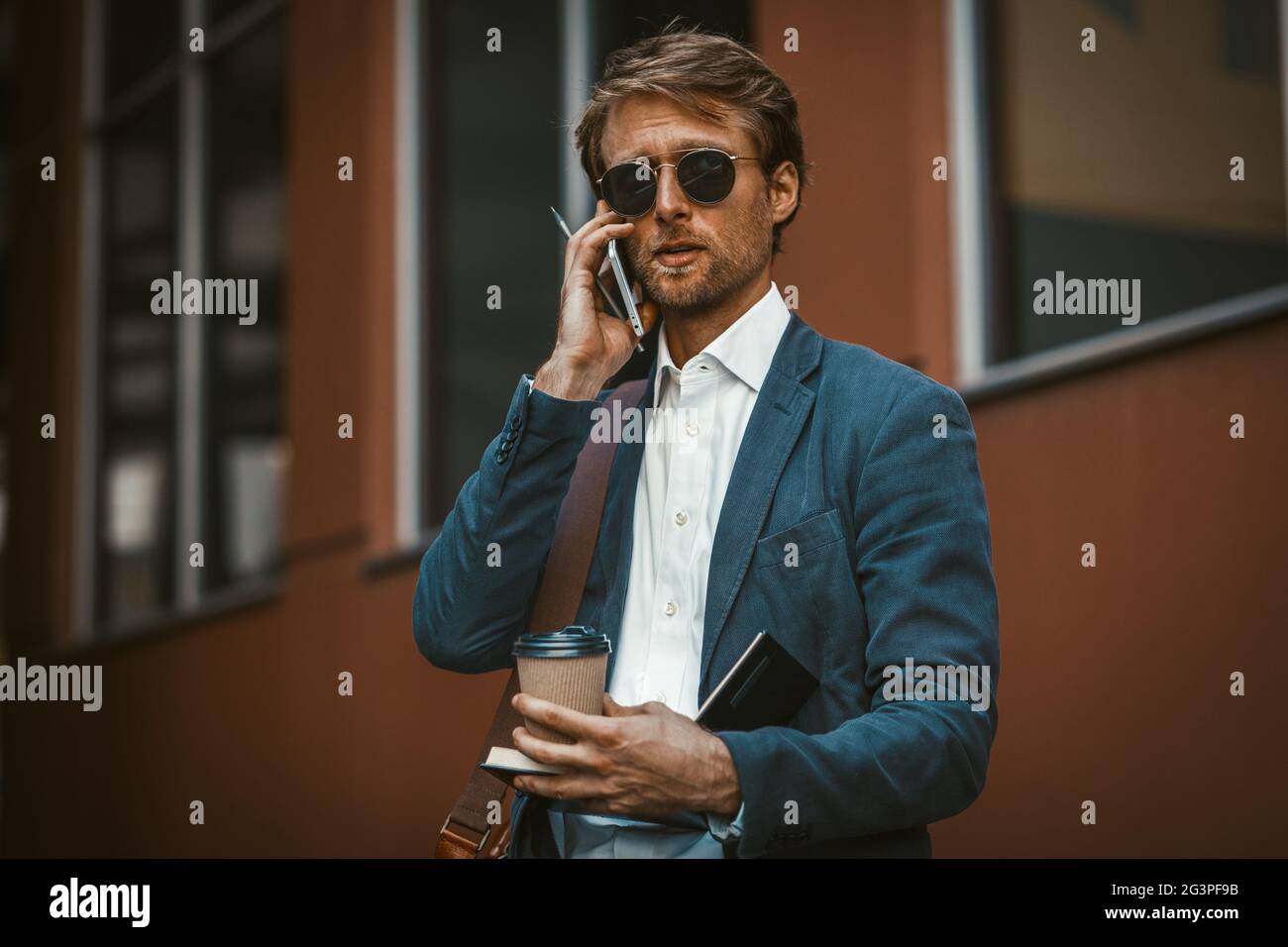 Gutaussehender junger Geschäftsmann mit Einwegbecher und Telefongespräch Stockfoto