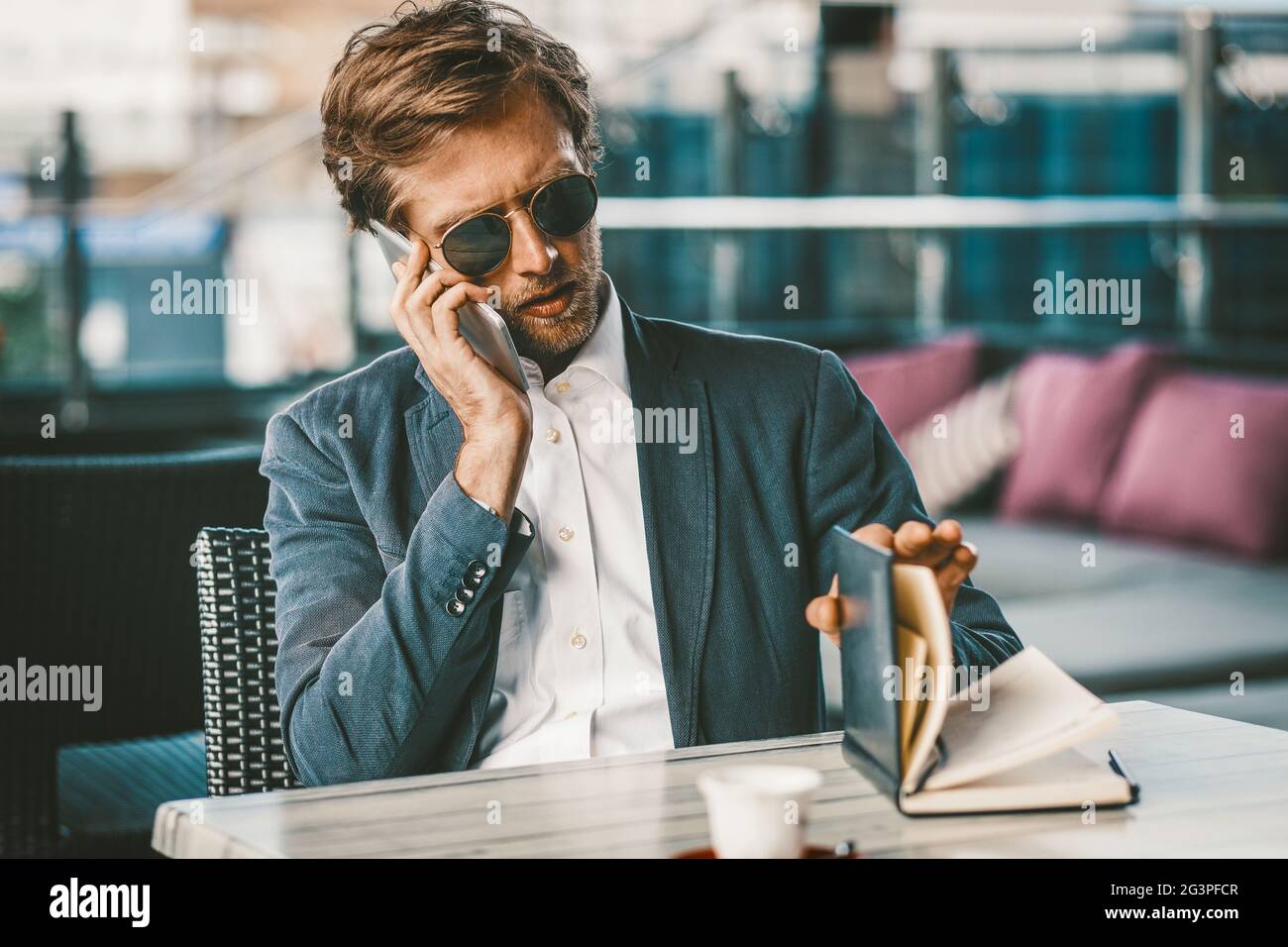 Der junge Geschäftsmann, der Terminkalender macht, ist während des Telefonsprechens sehr verbunden Stockfoto