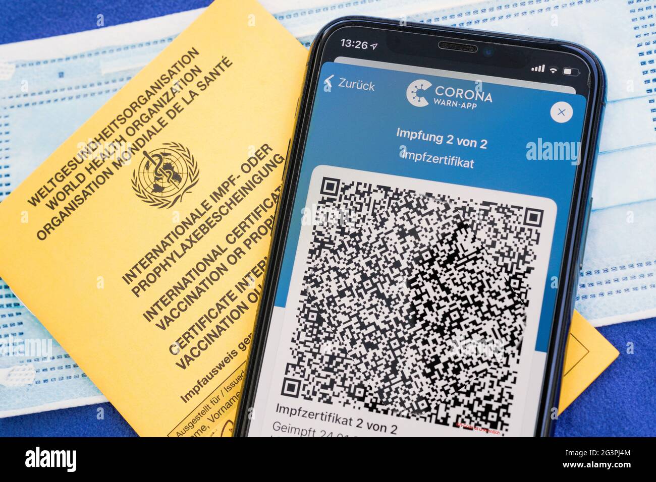 QR-Code, das digitale Impffzertifkat in der Corona Warn-App auf einem Smartphone bestätigt eine abgeschotene Impfung gegen Covid-19. Liegt auf dem gelben International Impfbescheinung, Impfpass. - ACHTUNG! QR-Code und persönliche Angaben sind unerklärlich gemacht! Stockfoto