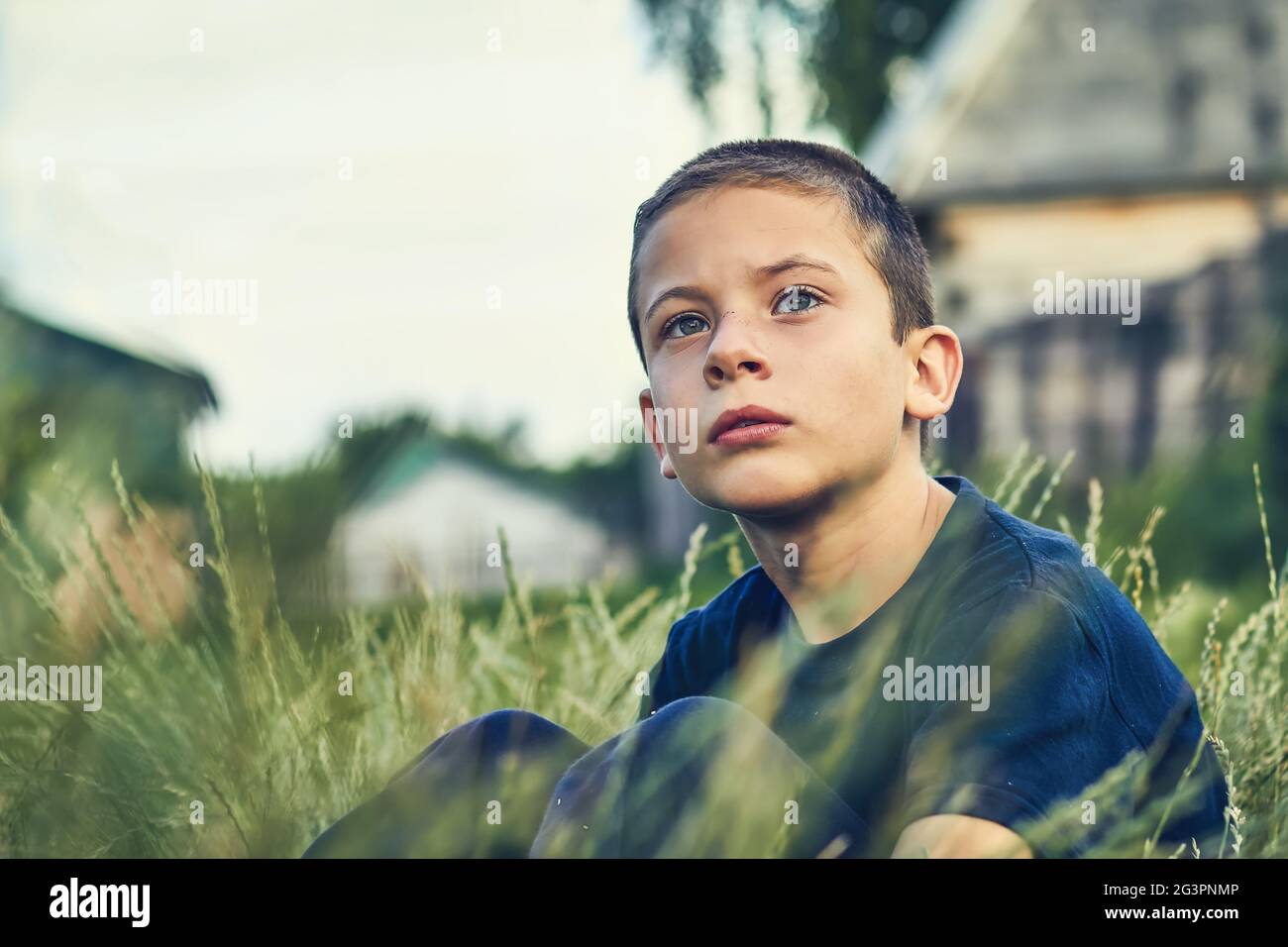 Das Kind sitzt im Gras im Freien und schaut ernsthaft in die Ferne. Stockfoto