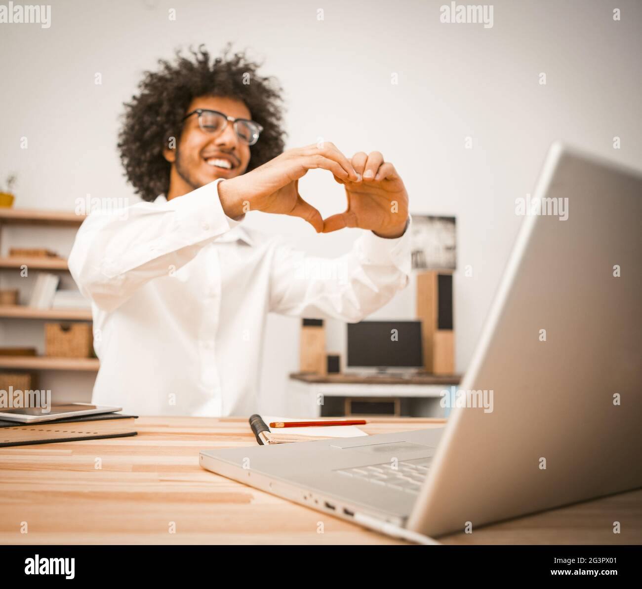 Der junge Mann führt einen Videoanruf durch und kommuniziert über einen Videolink mit Freunden. Arabischer Kerl zeigt ein Herzzeichen mit seinen Händen, die lo ausdrücken Stockfoto