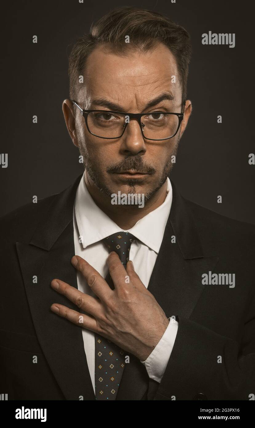 Ein intelligenter Geschäftsmann mit Brille richtet seine Krawatte gerade und blickt auf die Kamera. Nahaufnahme des erfolgreichen durchdachten Busins Stockfoto