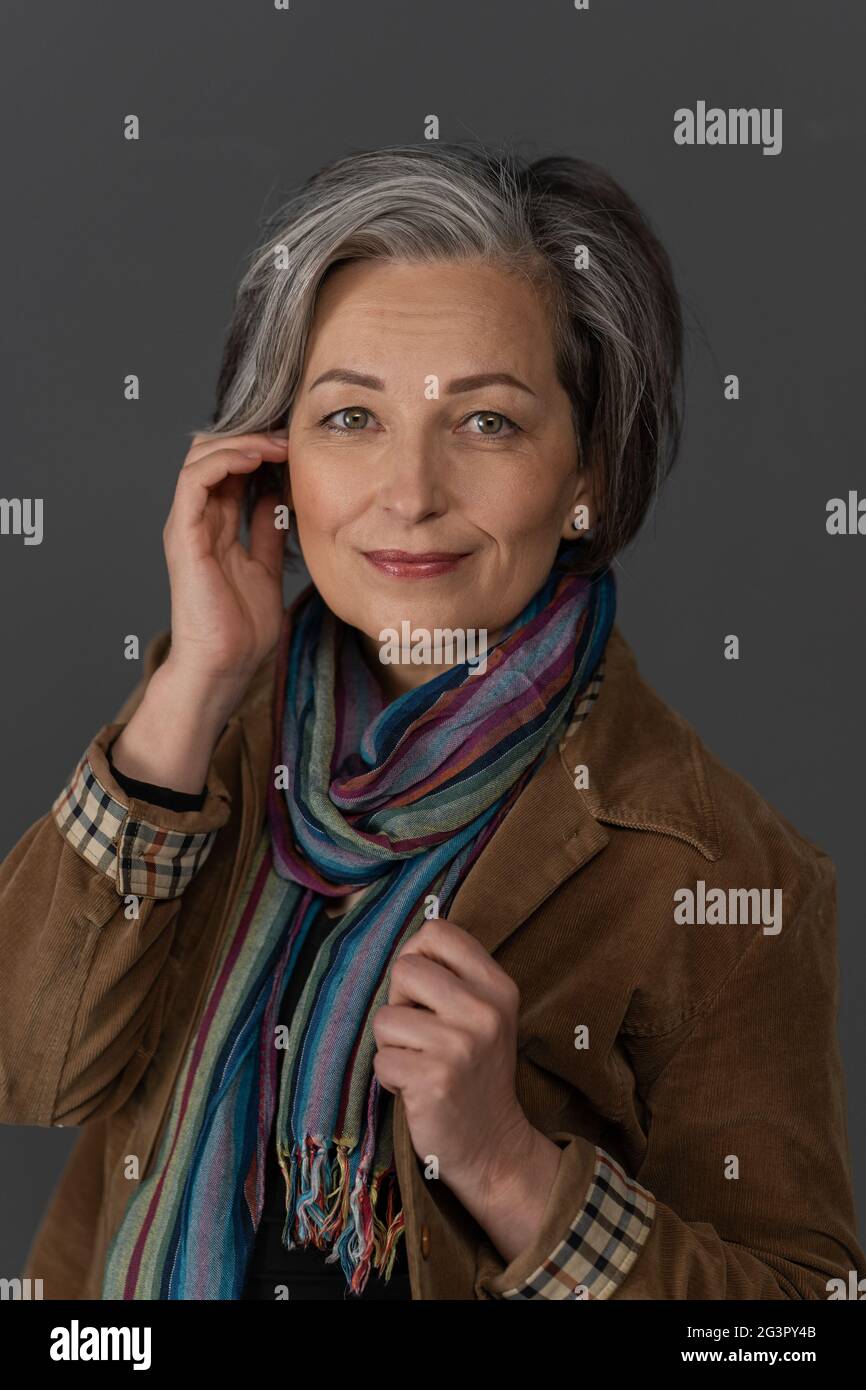 Stilvolle grau Frau charmant lächelt Blick auf die Kamera. Kaukasische Schönheit mittleren Alters in brauner Cordjacke mit Multi gekleidet Stockfoto