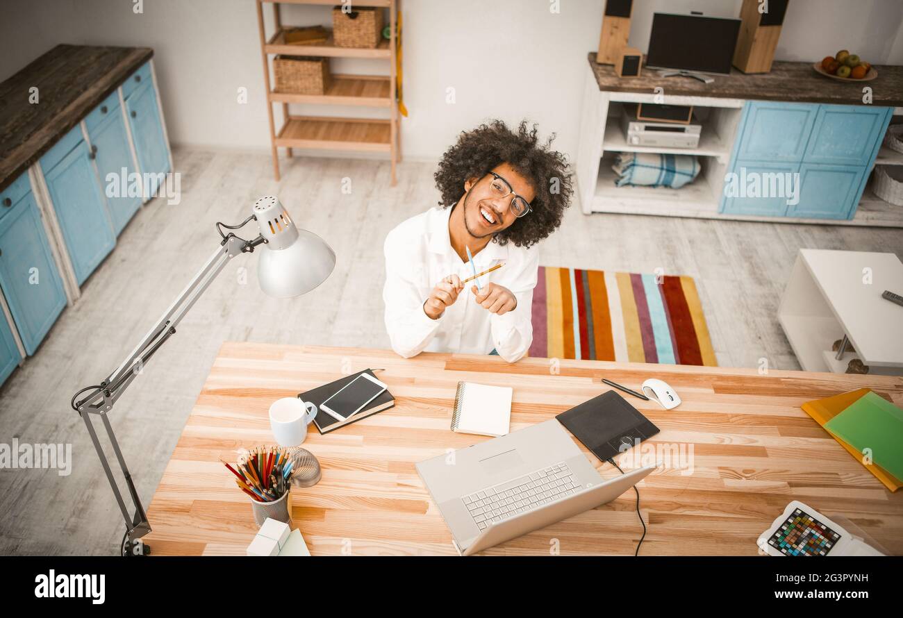 Der junge Geschäftsmann Jolly machte Pause von der Arbeit. Fröhlicher arabischer Typ spielt mit Bleistiften und schaut in die Kamera, während er am Arbeitsplatz sitzt Stockfoto
