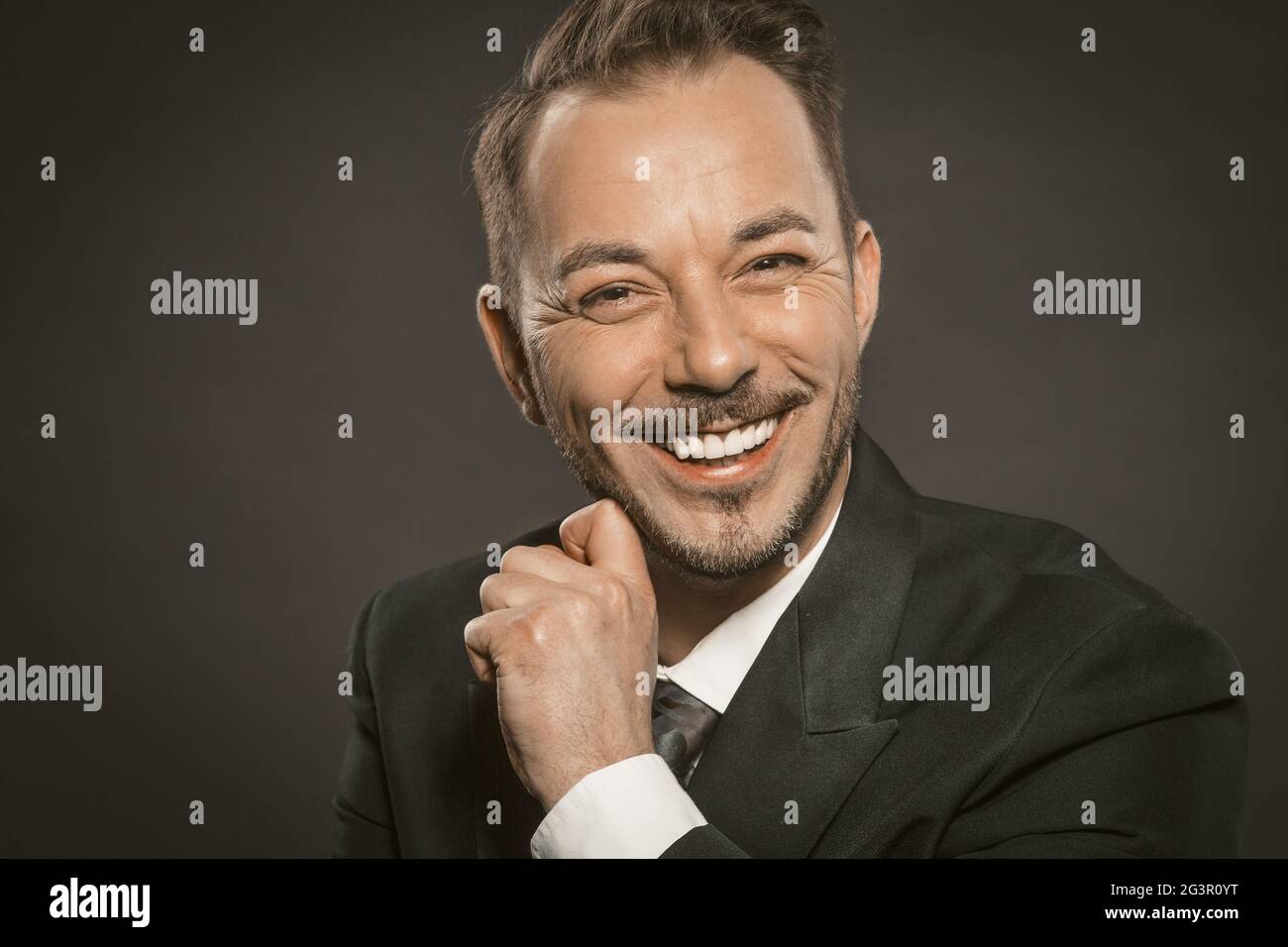 Ein fröhlicher Geschäftsmann lächelt breit und berührt seinen Bart und schaut in die Kamera. Nahaufnahme des kaukasischen gutaussehenden Mannes in for Stockfoto