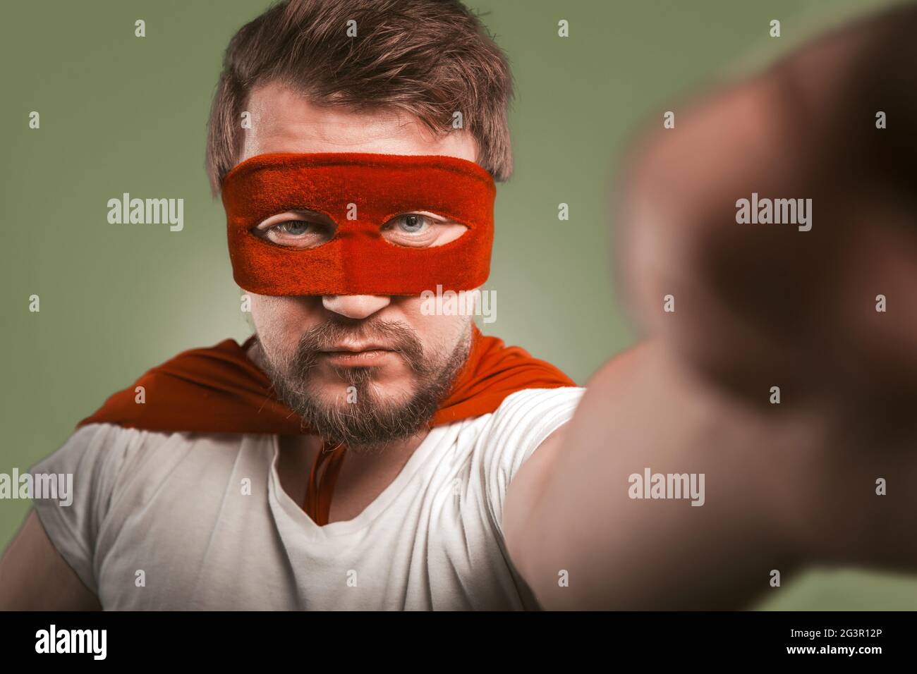 Superhelden Mann macht Selfie-Fotos oder Videos von Mobiltelefonen. Ernsthafter Mann mit roter Maske und Mantel, der für seinen sozialen Netwo posiert Stockfoto