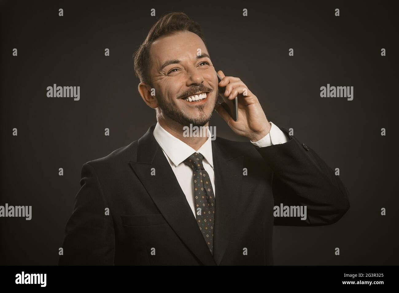 Ein fröhlicher Geschäftsmann lächelt auf dem Handy. Porträt eines vielbeschäftigten Büromitarbeiters mit Mobiltelefon. Kommunikationsdrahts Stockfoto