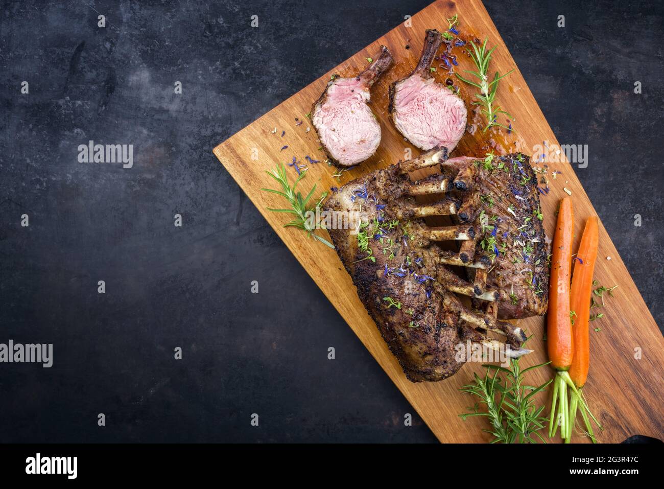 Grillrost aus Lamm mit Karotten und Kräutern als Draufsicht auf einem modernen Design Holzbrett mit Kopierplatz angeboten Stockfoto