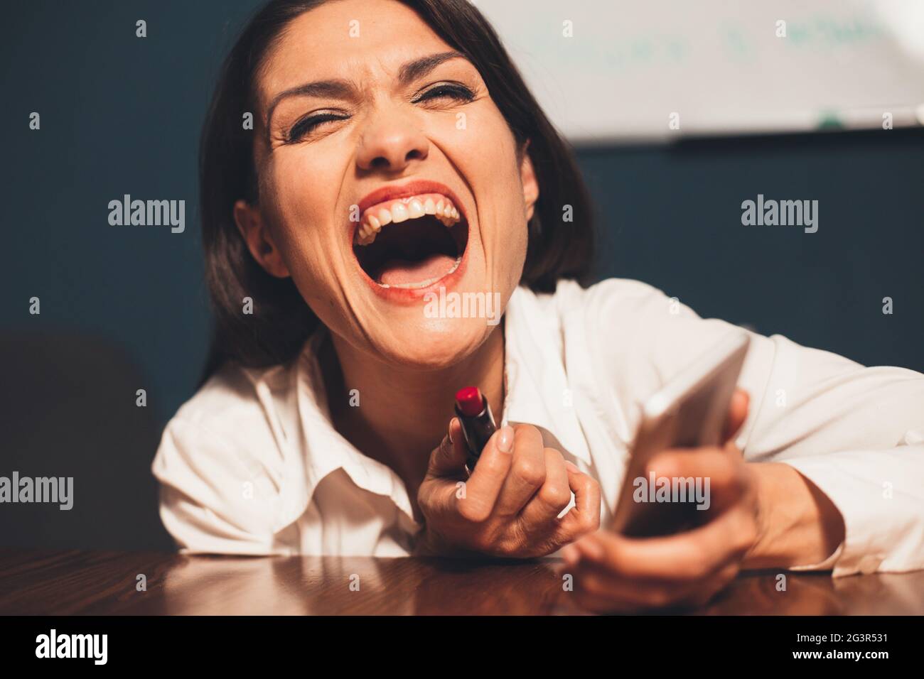 Junge verrückte Geschäftsfrau lacht Make-up mit rotem Lippenstift am Arbeitsplatz. Getöntes Bild Stockfoto