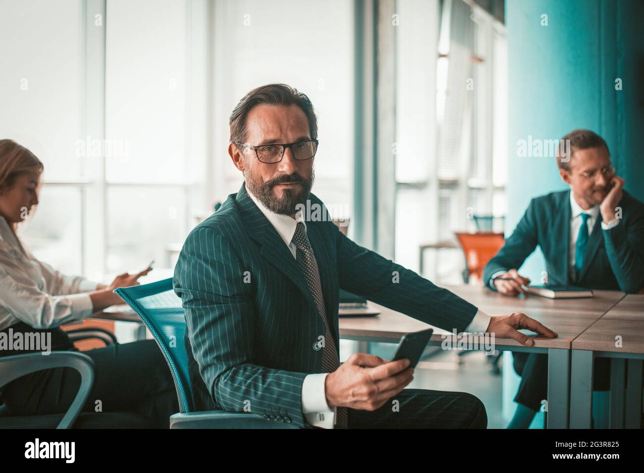 Selbstbewusster Geschäftsmann und kreatives Team, das im Büro arbeitet. Der männliche Projektleiter blickt vor dem Hintergrund von Kollegen auf die Kamera Stockfoto