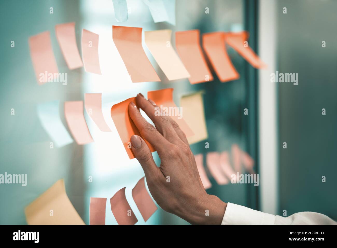 Die Hand der kaukasischen Frau klebt einen Aufkleber auf einem Fenster im Büro. Office Notes-Konzept. Hochwertige Fotos Stockfoto