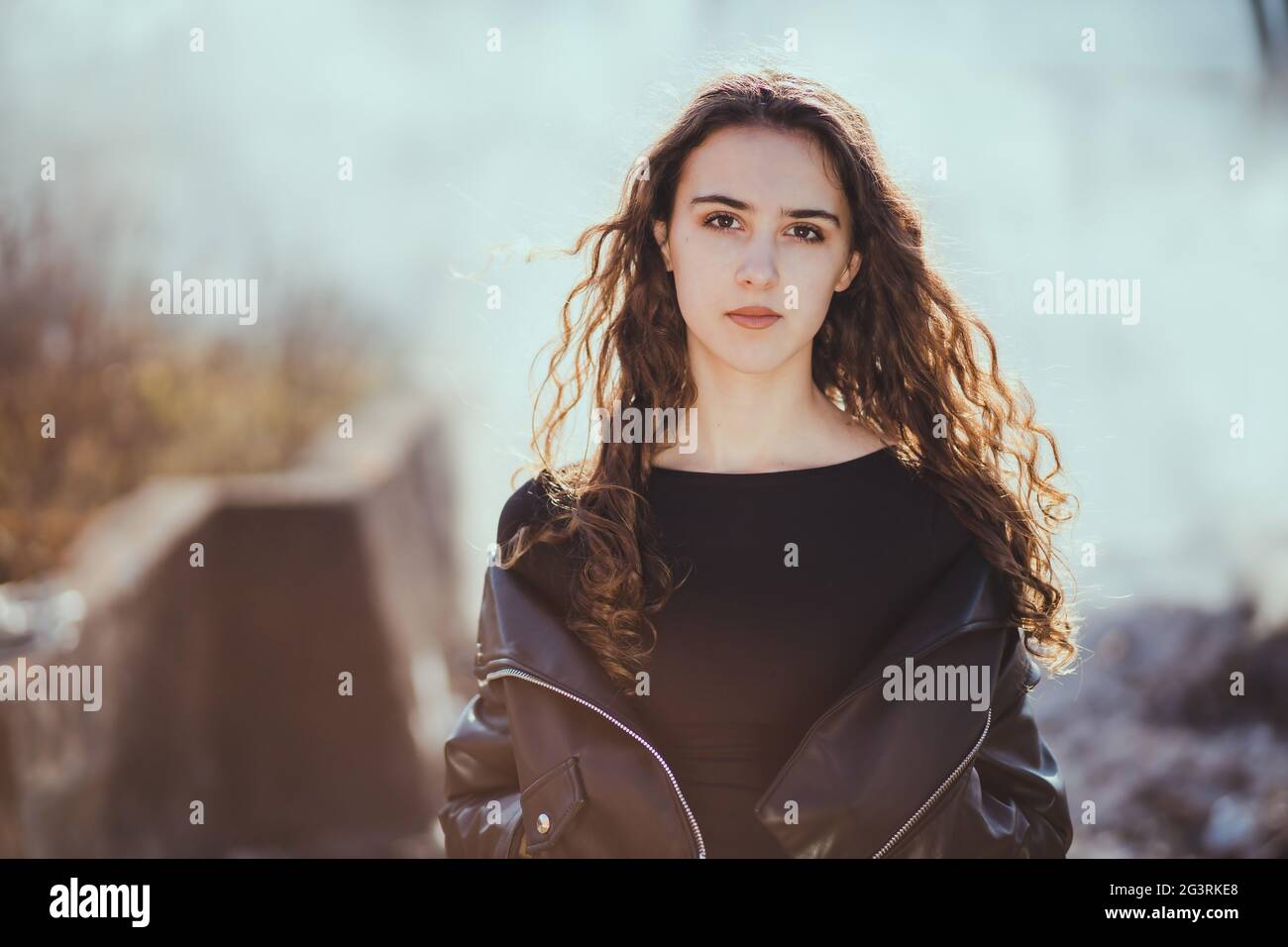 Outdoor-Porträt eines schönen Teenager Brünette Mädchen in der schwarzen Lederjacke mit Rauch im Hintergrund Stockfoto