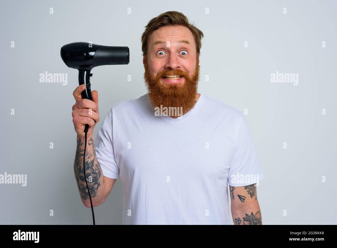 Glücklicher Mann mit Bart spielen mit Haar dryeras eine Pistole Stockfoto
