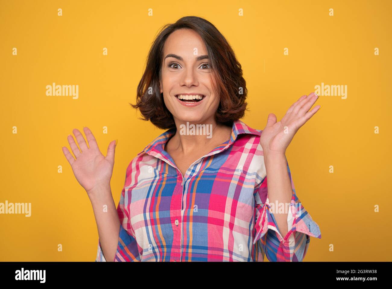 Enthusiastische Frau, die ihre Hände hochhebt. Lächelnd junge Brünette in casual ausgeschnitten auf gelbem Hintergrund Stockfoto