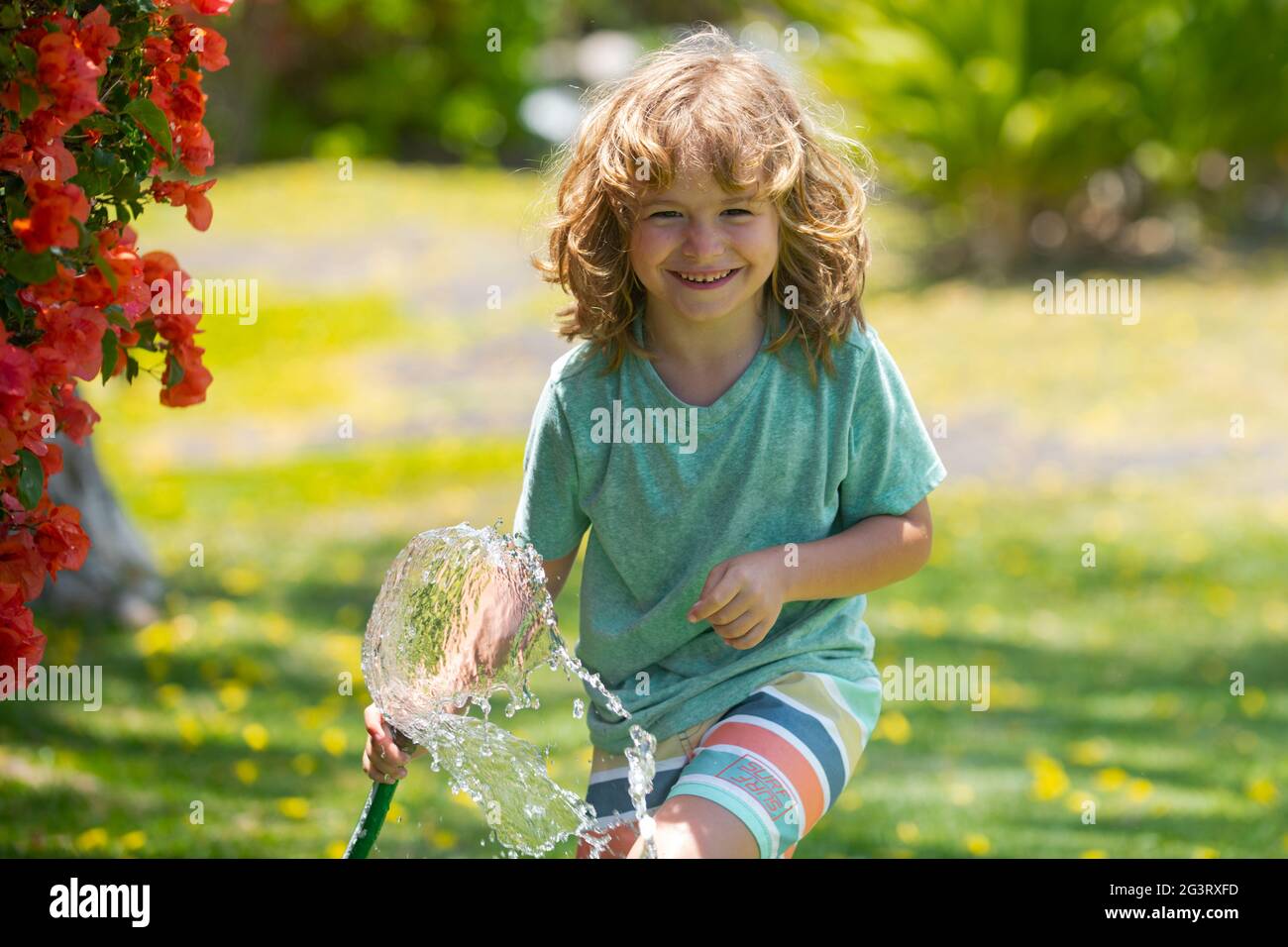 Süßer kleiner Junge, der am Sommertag Blumen im Garten wässert.  Kinderbauernin mit Gartenschlauch in Pflanzpflanze. Schlauch. Lustige Kind  Bewässerung Pflanzen in der Stockfotografie - Alamy