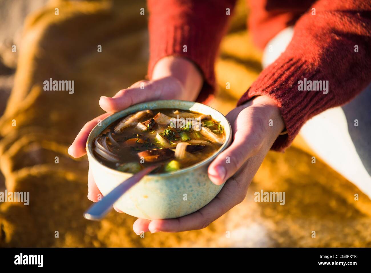 Junge Frau genießt Suppe, während sie alleine am Strand campen Stockfoto
