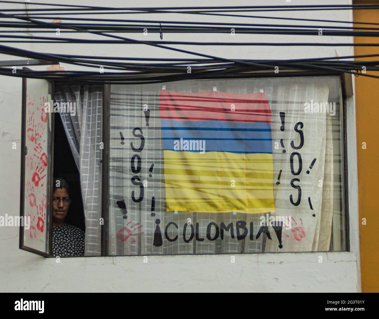Pasto, Kolumbien. Juni 2021. Eine Frau sieht aus ihrem Fenster mit einer kolumbianischen Flagge auf dem Kopf und der Botschaft „S.O.S Colombia“, wie regierungsfeindliche Proteste gegen Präsident Ivan Duque, Ungleichheiten und Polizeibrutalität in Kolumbien am 16. Juni 2021 in Pasto, Narino, Kolumbien, zu ihrem siebenten Admisten von mindestens 70 Toten aufsteigen. Quelle: Long Visual Press/Alamy Live News Stockfoto