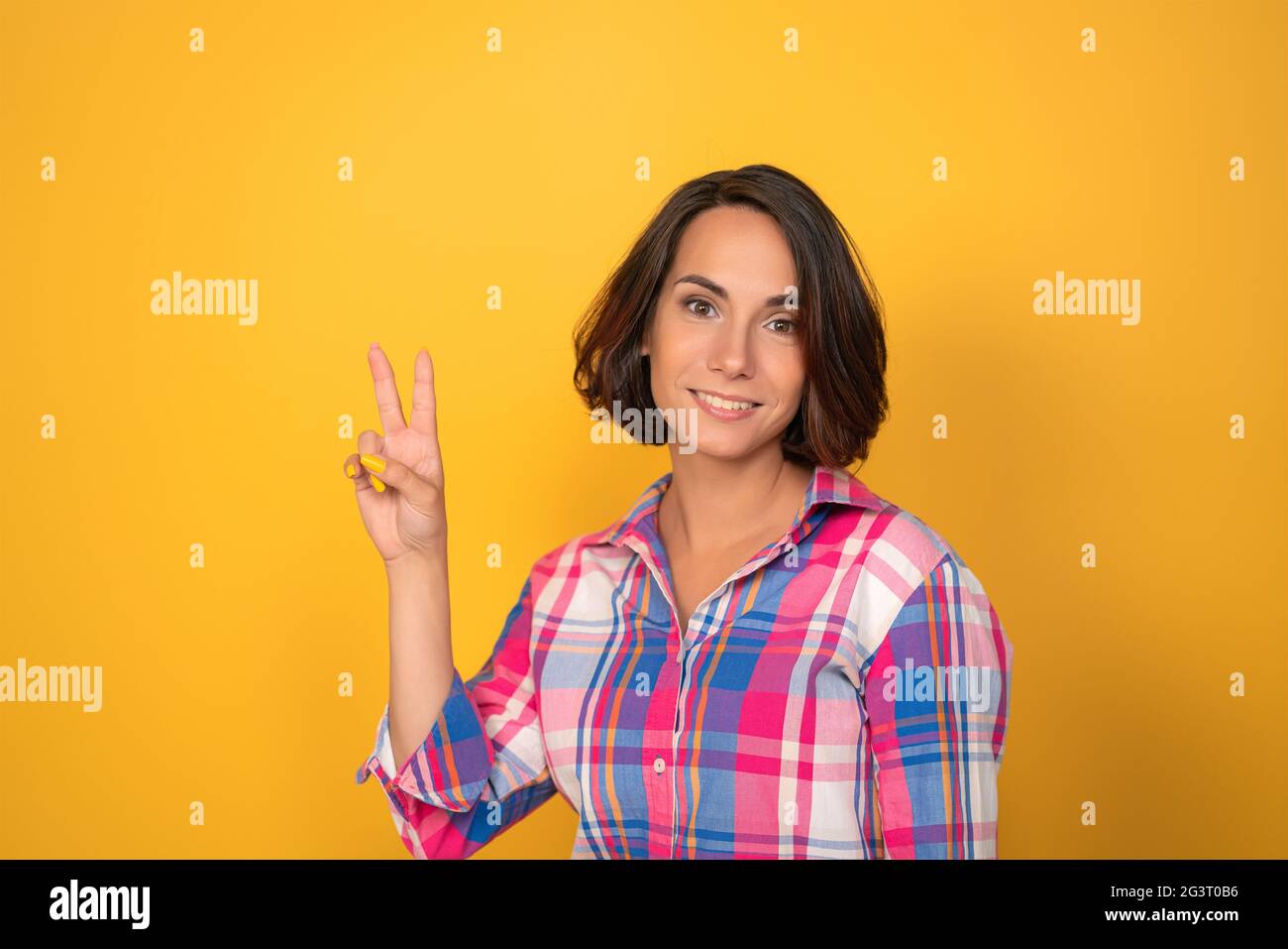 Die junge Frau zeigt das Zeichen des Friedens an ihren Händen Auf gelbem Hintergrund Stockfoto