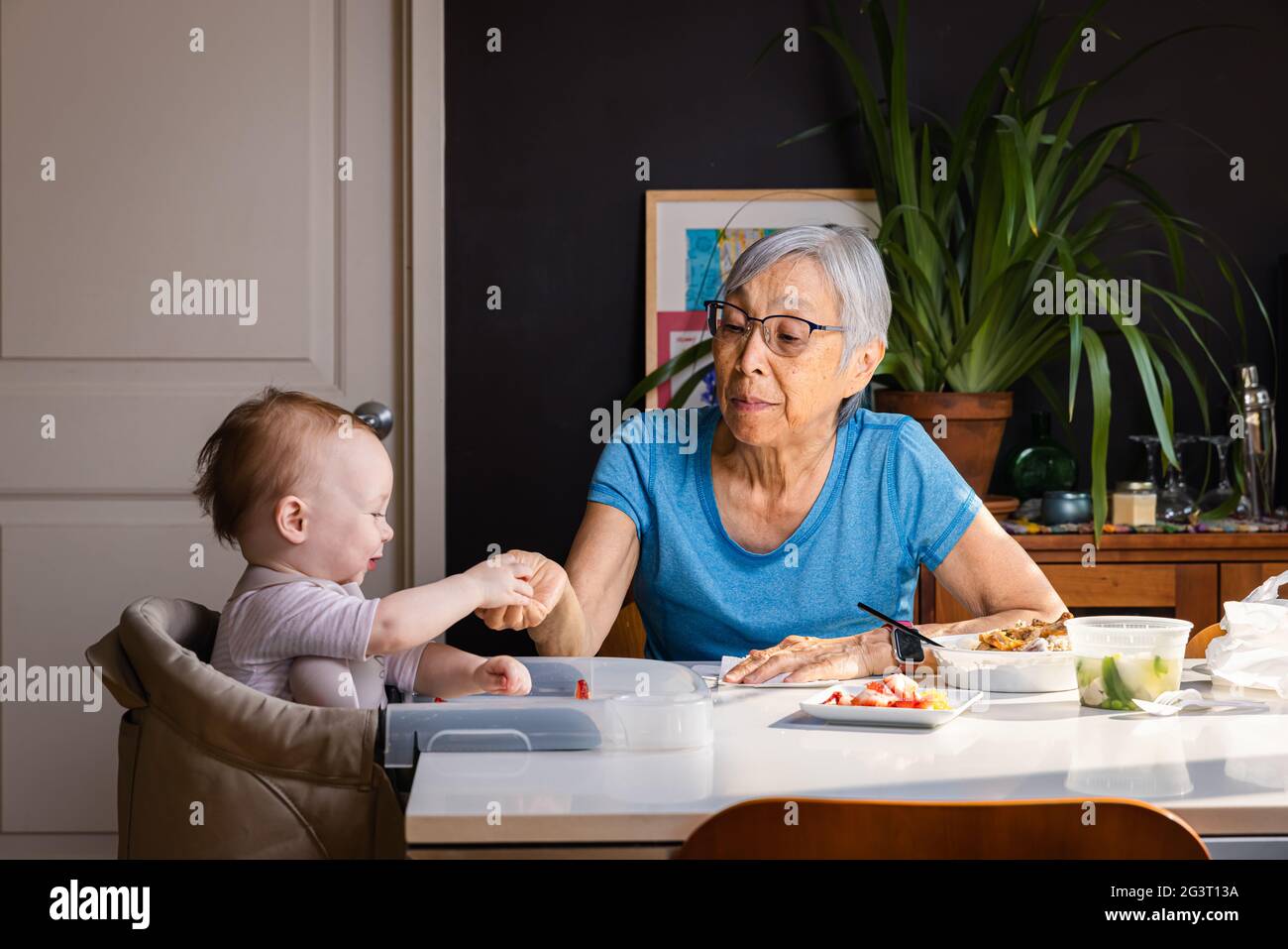 Ältere asiatische Frau füttert Kleinkind Enkelin am Tisch zu Hause Stockfoto