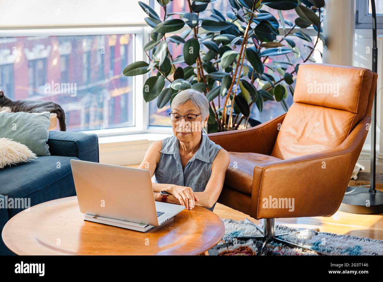 Ältere asiatische Frau sitzt und mit Laptop zu Hause im Wohnzimmer Stockfoto