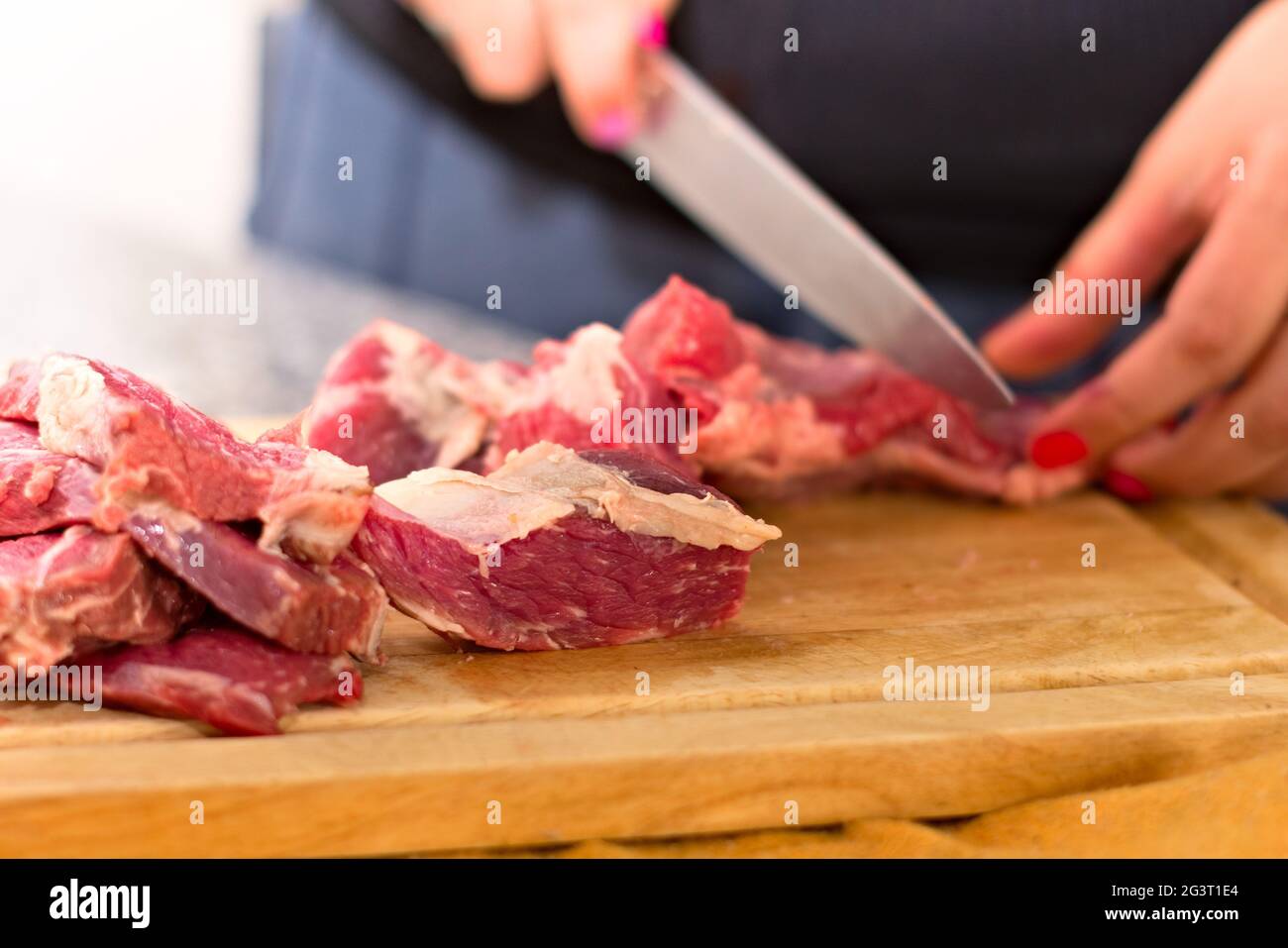 Frau schneidet Fleisch auf einem hölzernen Schneidebrett. Nahaufnahme. Stockfoto