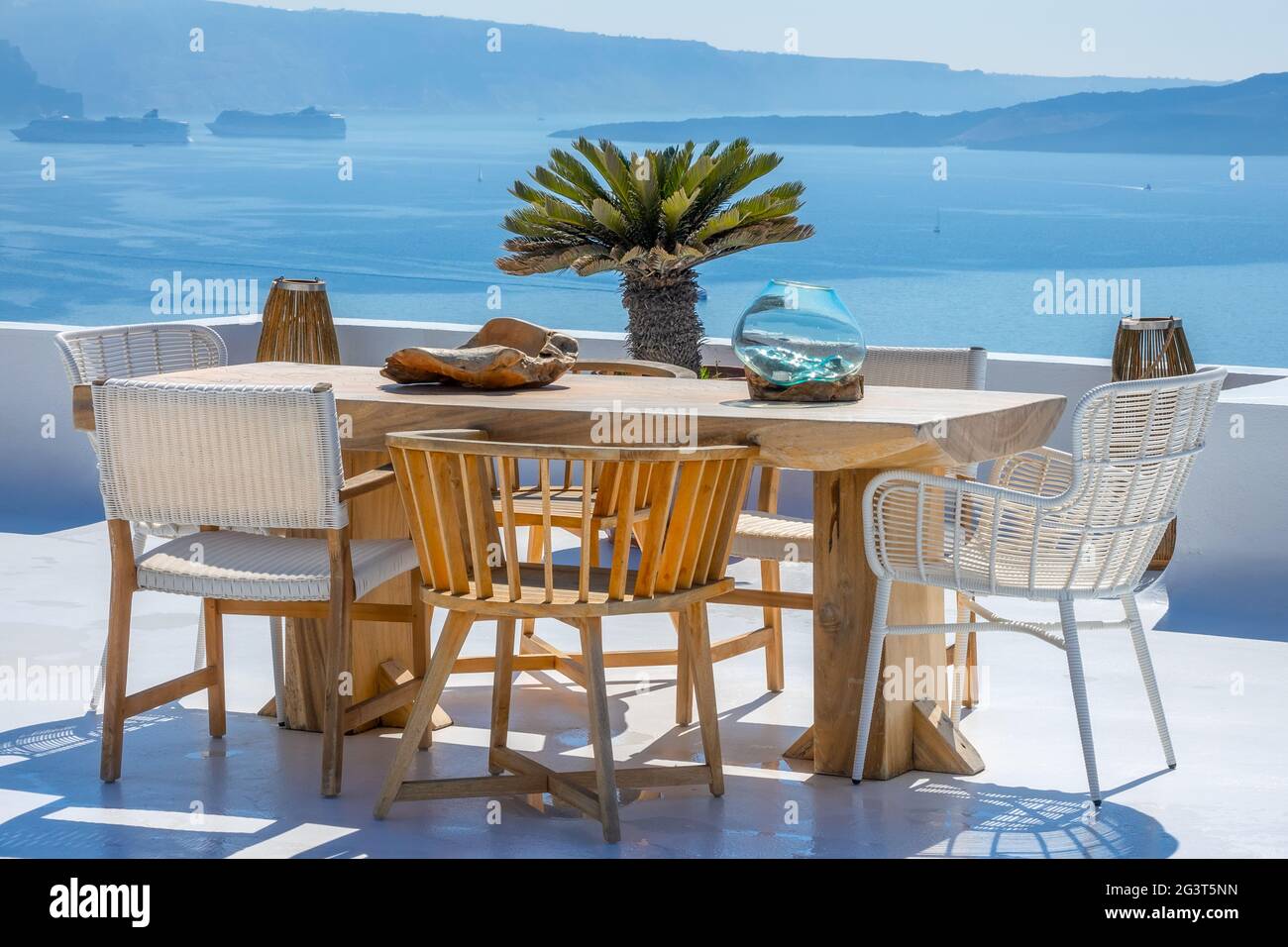 Holztisch und -Stühle auf einer Sonnenterrasse mit Blick auf das Meer und die Schiffe Stockfoto