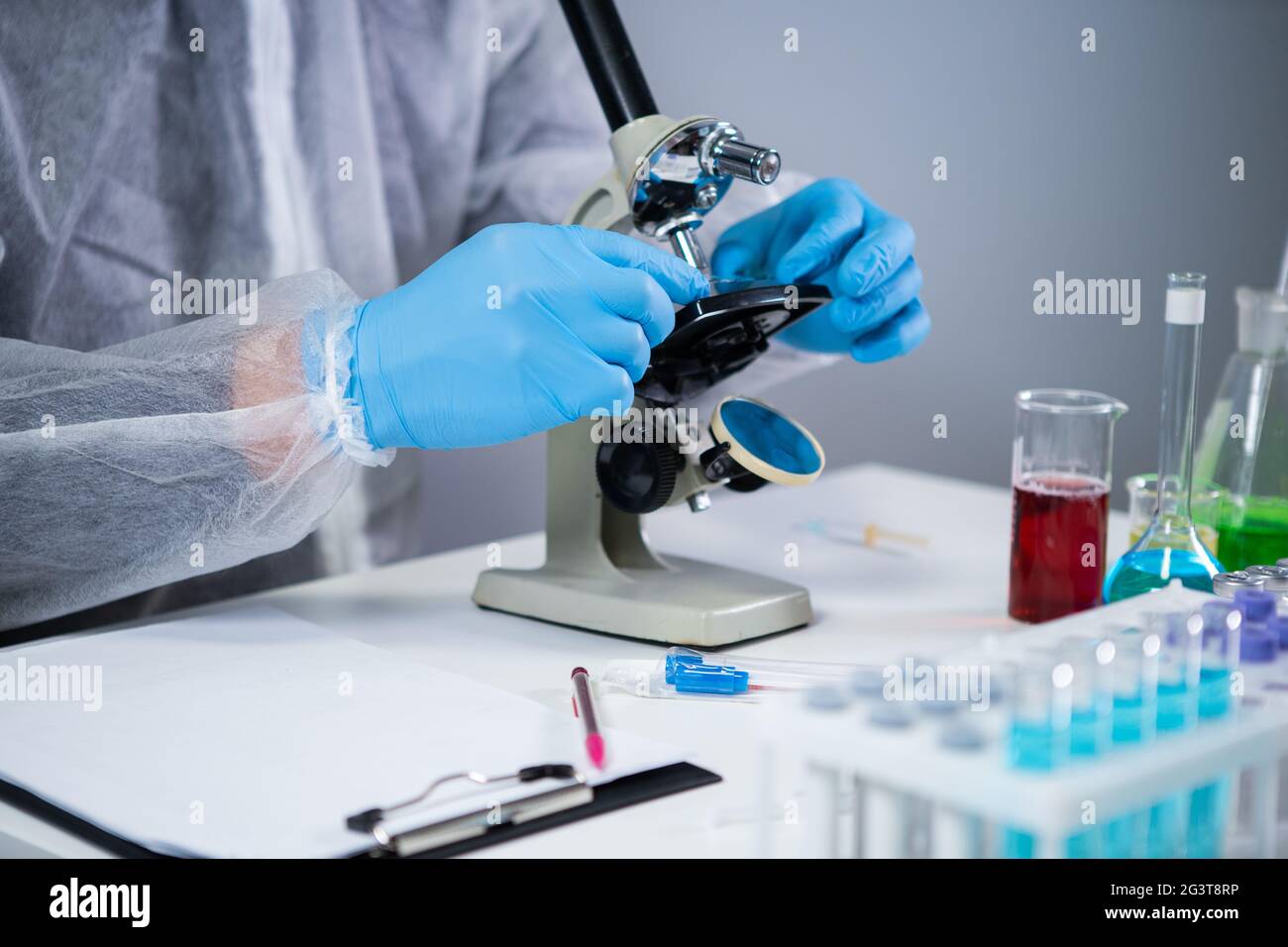 Medizinischer Fachmann in weißem Schutzanzug, der im chemischen Labor durch das Mikroskop schaut. Suchen Sie nach Impfstoff-Coronavirus. Cov Stockfoto