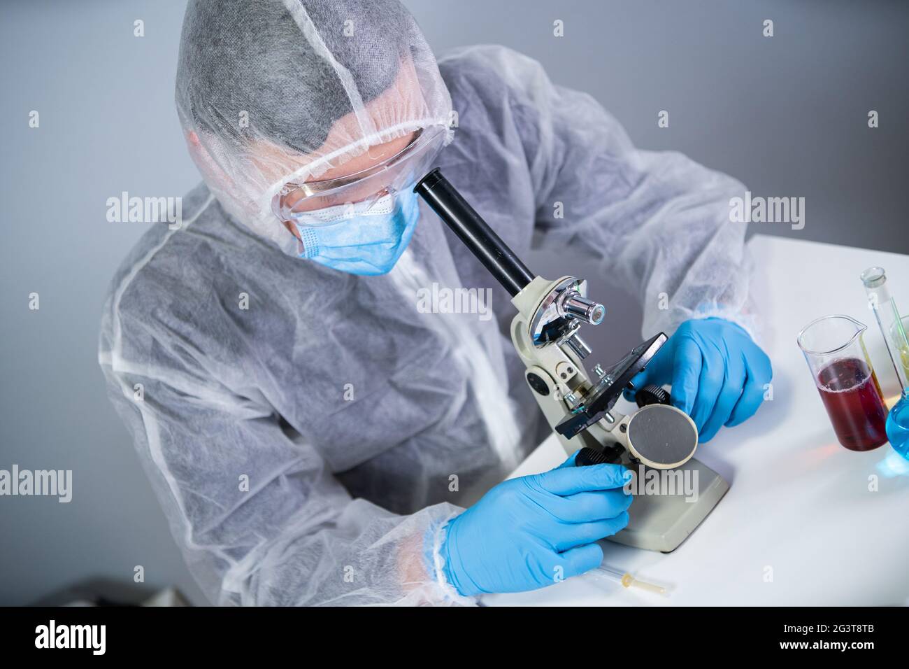 Wissenschaftler untersuchen Probe mit einem Mikroskop und betreiben medizinische Forschung im Wissenschaftslabor. Männlicher Laborassistent in Protect Stockfoto