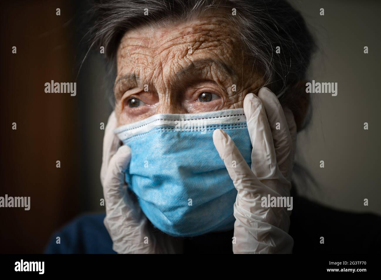 Porträt ältere Frau mit Kopfhänden, traurig besorgt Emotion in schützende medizinische Maske, Handschuhe gegen Virus und Infektion an Stockfoto