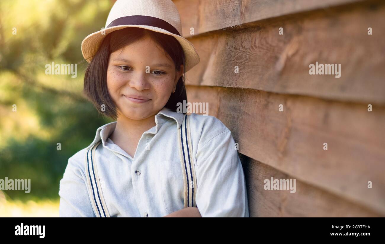 Ein schönes Mädchen in einem Hut und Hemd mit Hosenträger Steht lehnt an einem Holzhaus oder Scheune schaut Die Kamera Stockfoto