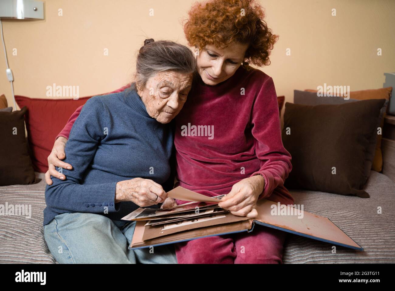 Positive gealterte Damen suchen Albumfotos Sofa zu Hause sitzend, fröhliche Freunde. Ältere Frau und ihre reife Krankenschwester beobachten pho Stockfoto