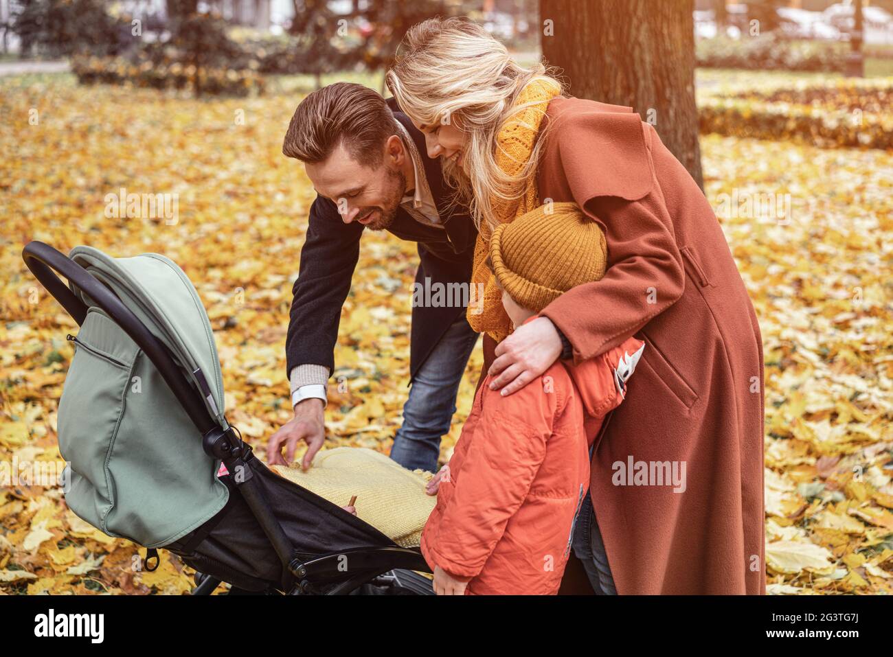 Eine junge Familie geht mit einem Sohn und einem Neugeborenen im Kinderwagen in einem Herbstpark spazieren. Familie im Freien in einem goldenen Herbstpark Stockfoto