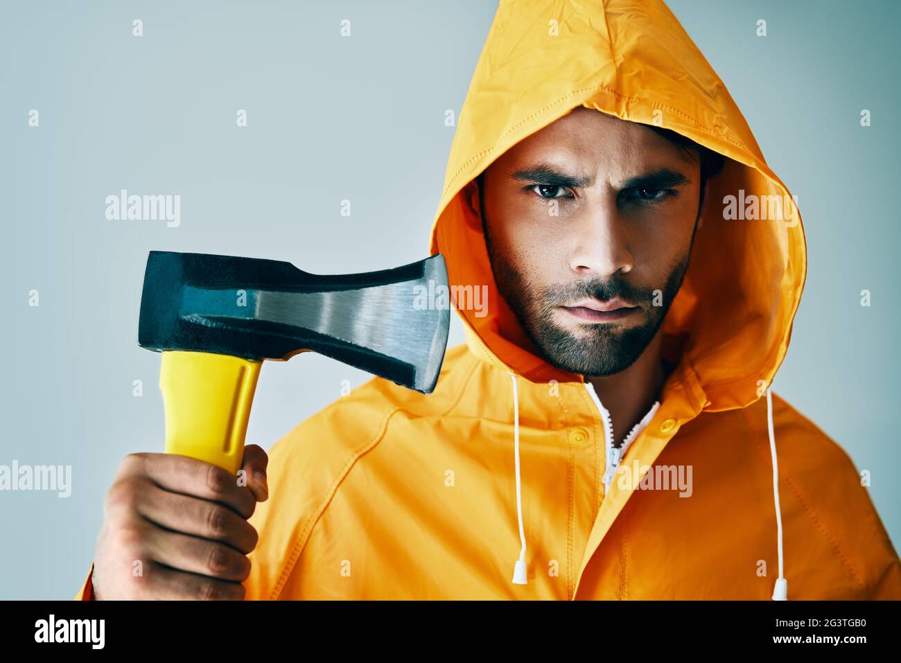 Porträt eines brutalen, gutaussehenden Mannes in einem hellen Regenmantel mit einer großen Axt Stockfoto