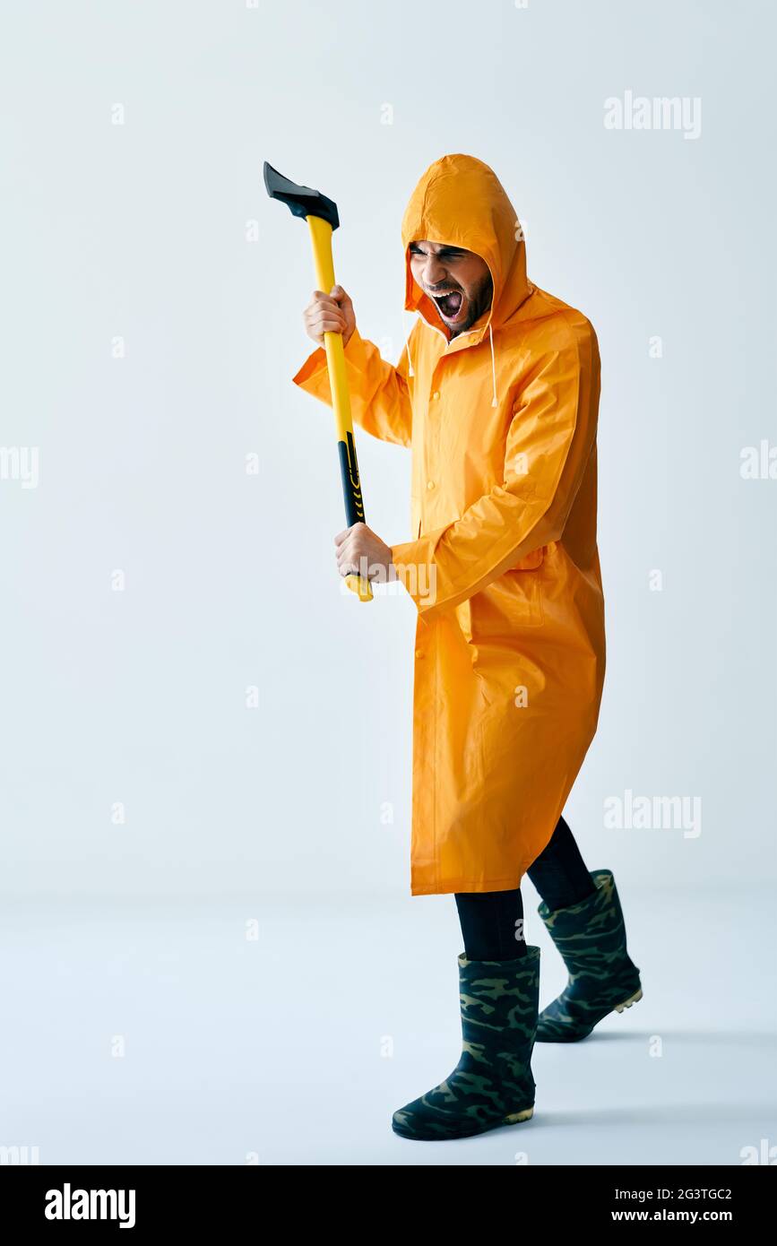 Aggressiver Mann im orangen Regenmantel droht mit Axt Stockfoto