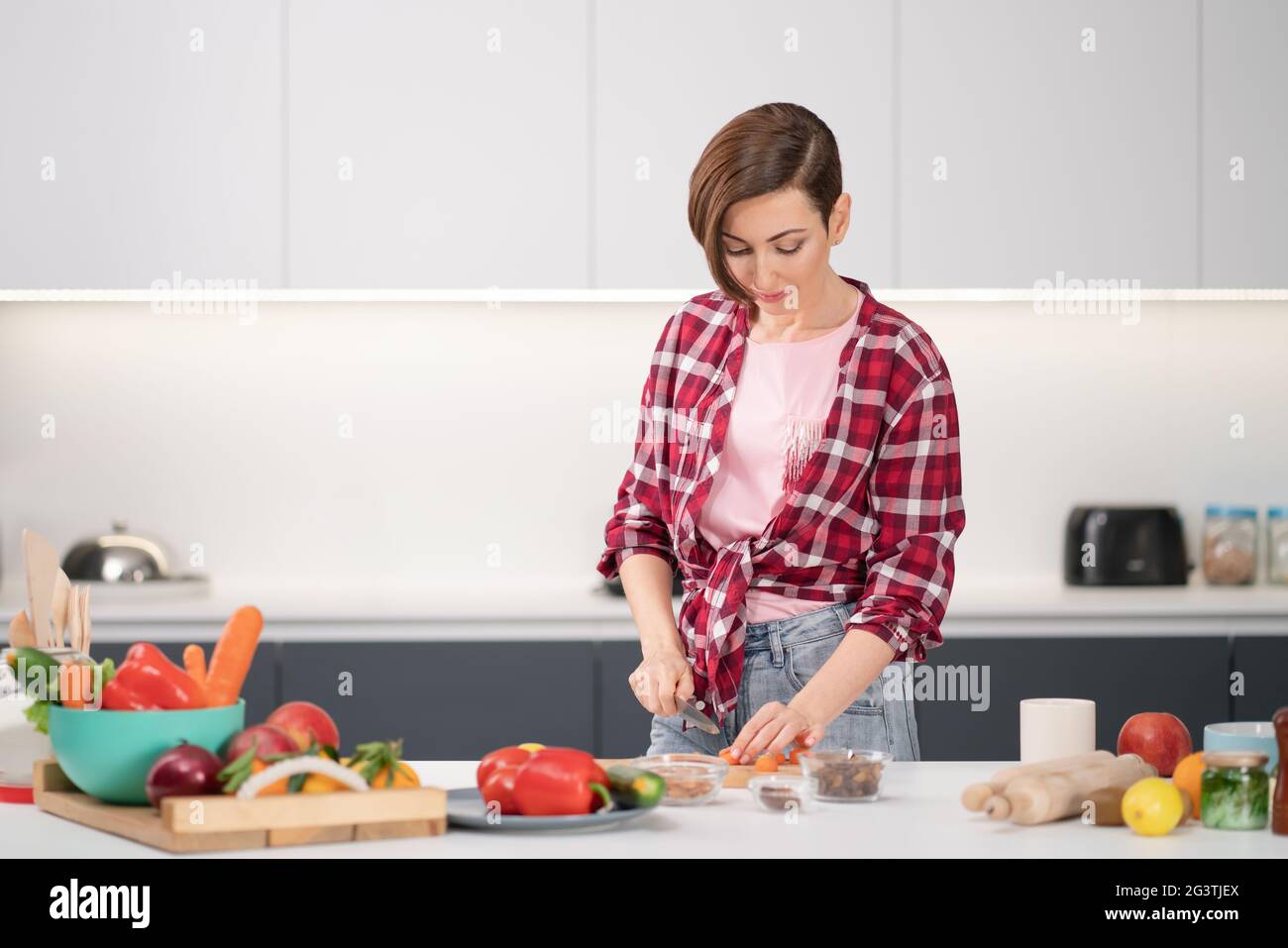 Kochen zu Hause für die liebevolle Familie. Hübsche junge Frau schneidet Zutaten auf dem Tisch und kocht ein Mittag- oder Abendessen im Set Stockfoto