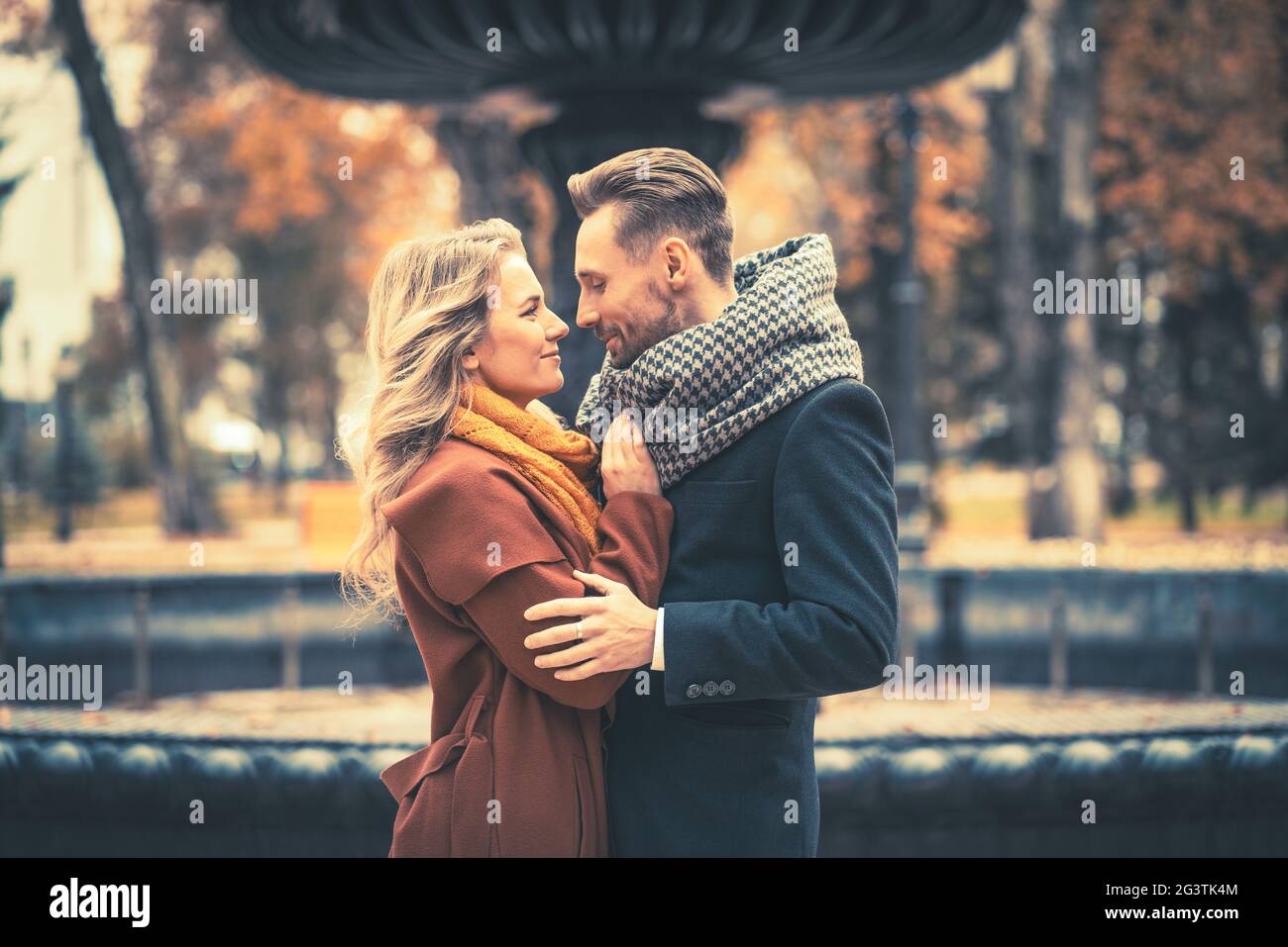 Nahaufnahme. Liebende junge Menschen, die umarmt stehen und sich in der Nähe eines alten Brunnens im Herbstpark anguchten, tragen sich Stockfoto