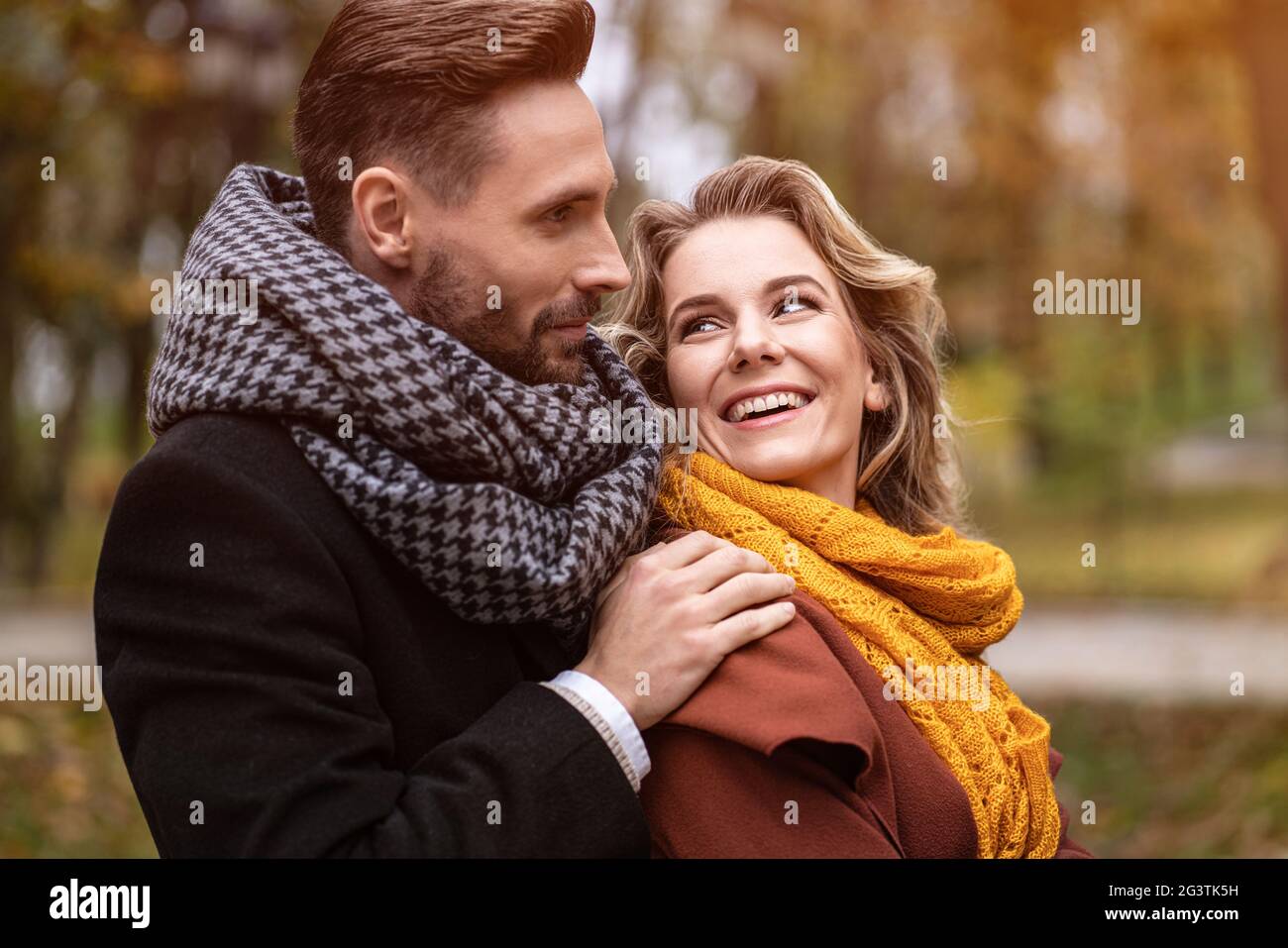Nahaufnahme. Glücklich in der Liebe junger Menschen, Mann umarmt Frau von hinten, als sie ihn ansieht, glückliches Paar, das in einem Herbstpark läuft Stockfoto