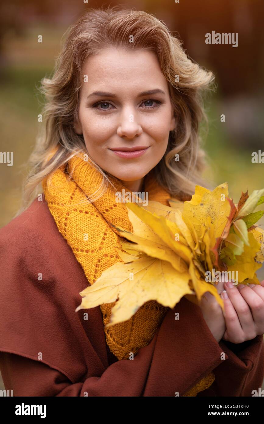 Schöne junge Frau posiert für die Kamera mit Herbstblättern in der Hand und Herbst gelben Garten oder Park. Schöne lächelnde junge Frau Stockfoto