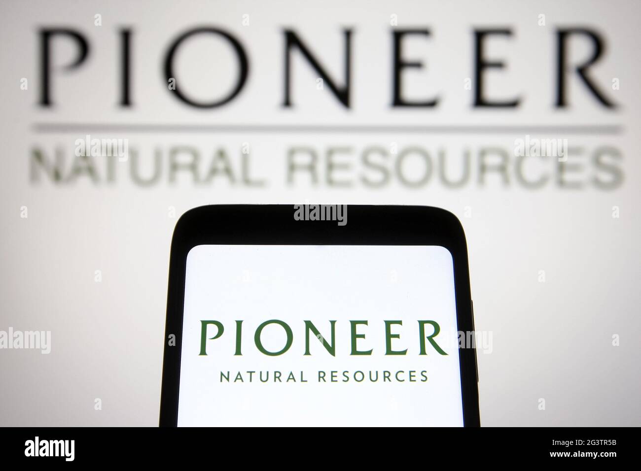 In dieser Abbildung ist das Logo des Unternehmens Pioneer Natural Resources auf einem Smartphone und einem pc-Bildschirm im Hintergrund zu sehen. Stockfoto