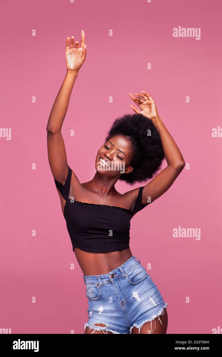 Tanzen mit Händen bis wunderschöne junge afroamerikanische Mädchen mit Afro-Haar posiert in schwarzen Top und Denim Jeans auf schmutzigen p gekleidet Stockfoto