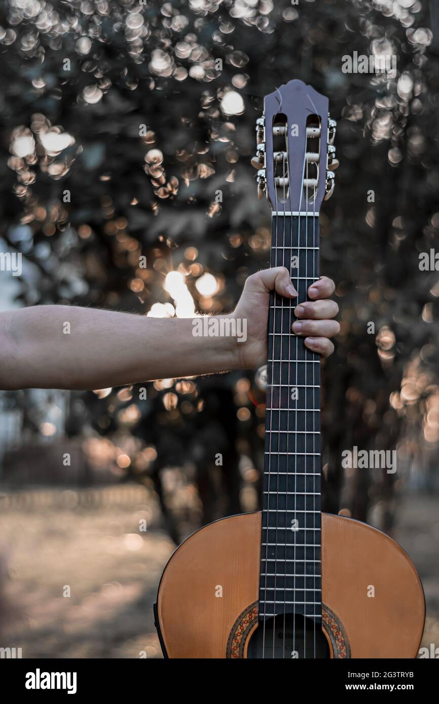 Mann hält Hals klassische Gitarre im Park mit Bokeh hellen Hintergrund, Nahaufnahme im Freien Stockfoto