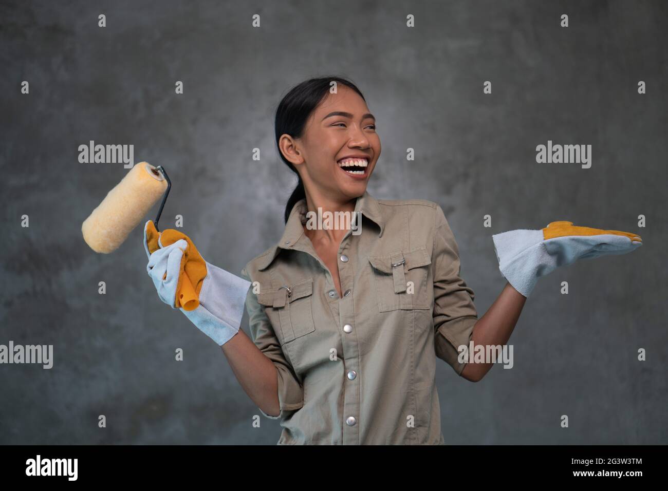 Attraktive junge Mädchen Baumeister mit Malrolle lächelnd über Betonwand Hintergrund Stockfoto