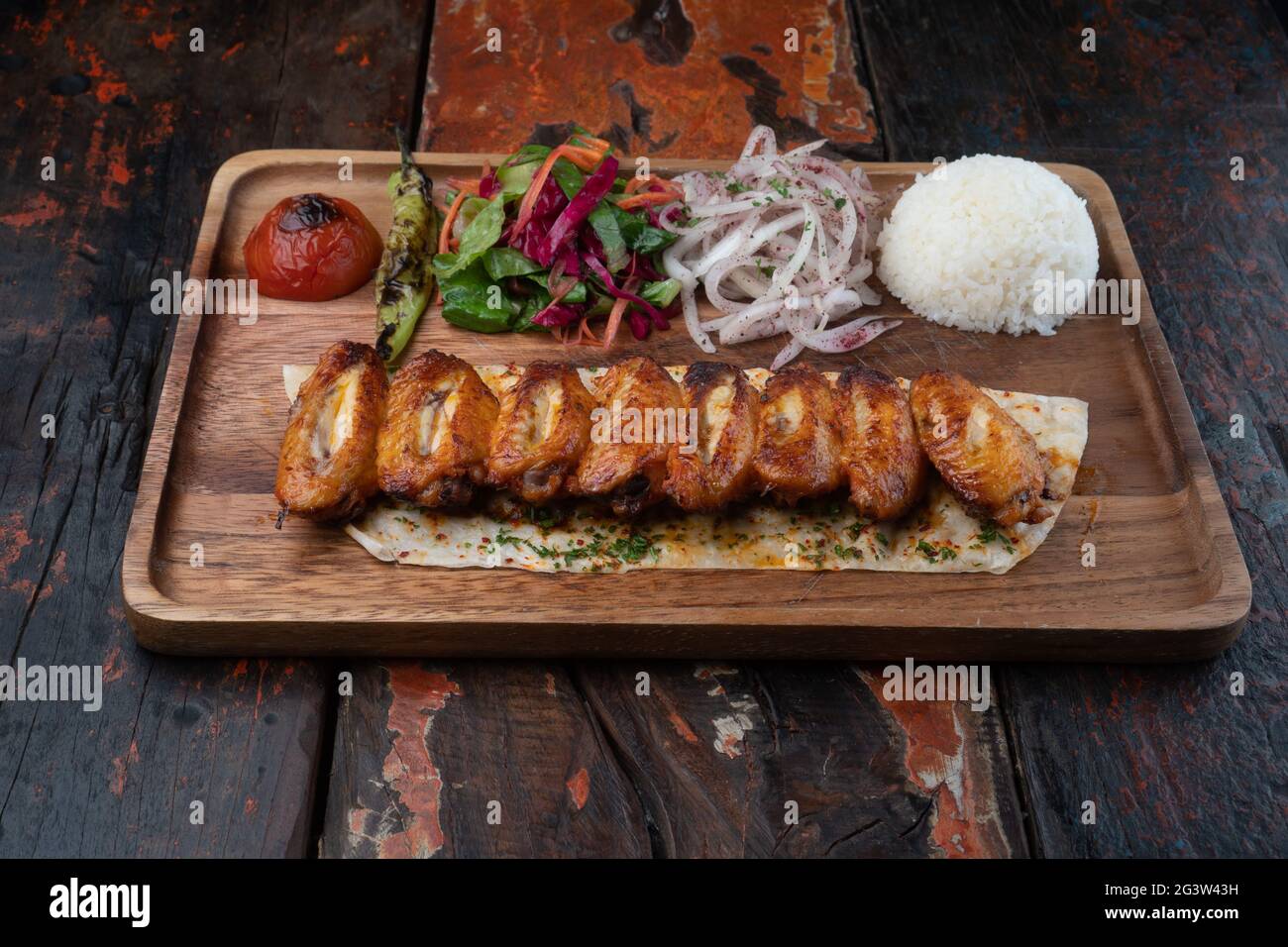 Türkische Hähnchenflügel oder Rinderkebab mit Reis und Gemüse auf rustikalem Holztisch Stockfoto