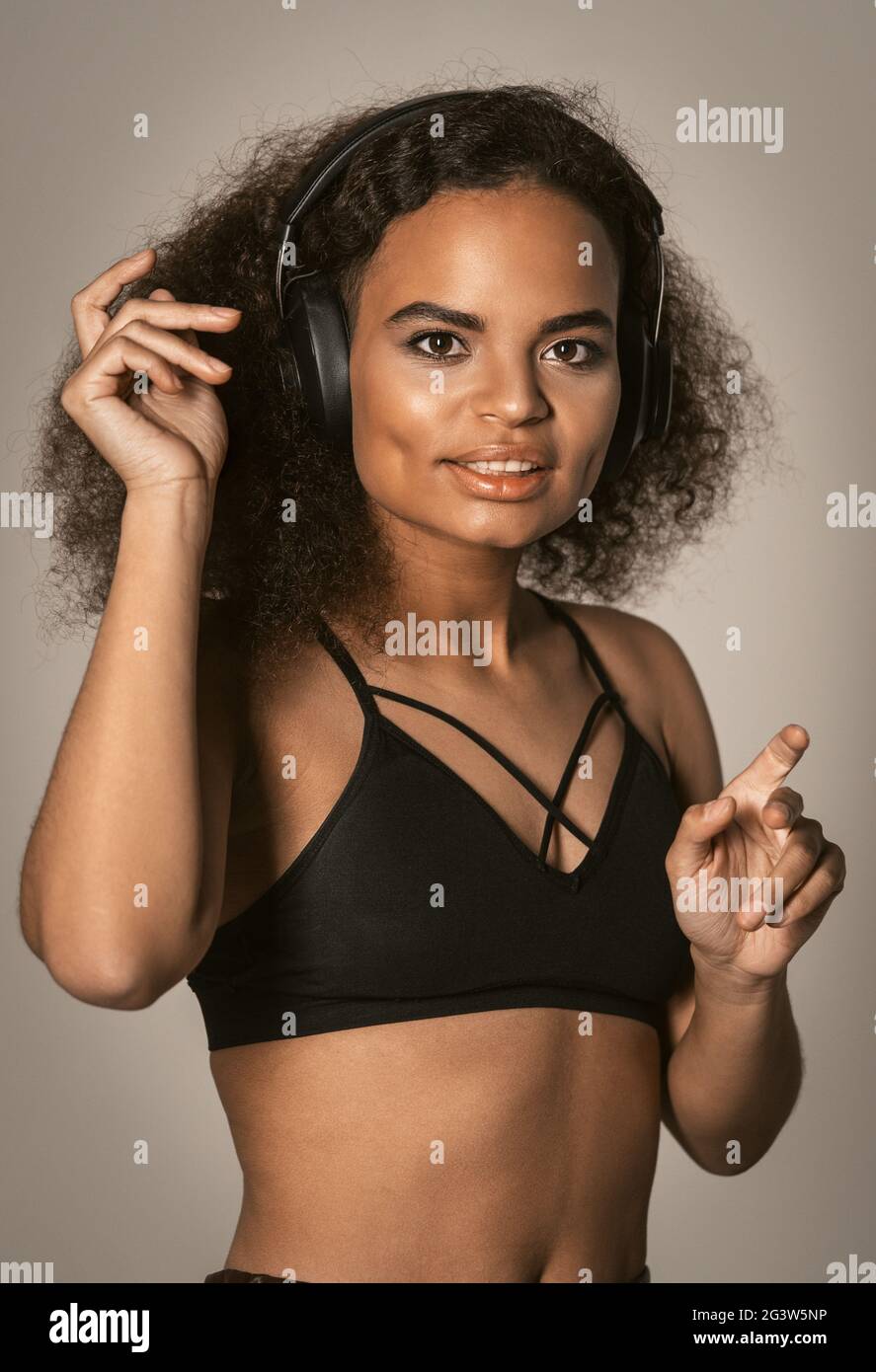 In Kopfhörern tanzend, hört das junge afroamerikanische Mädchen Musik in schwarzem Top und macht Salsa-Bewegungen mit den Händen in der Luft, Stockfoto