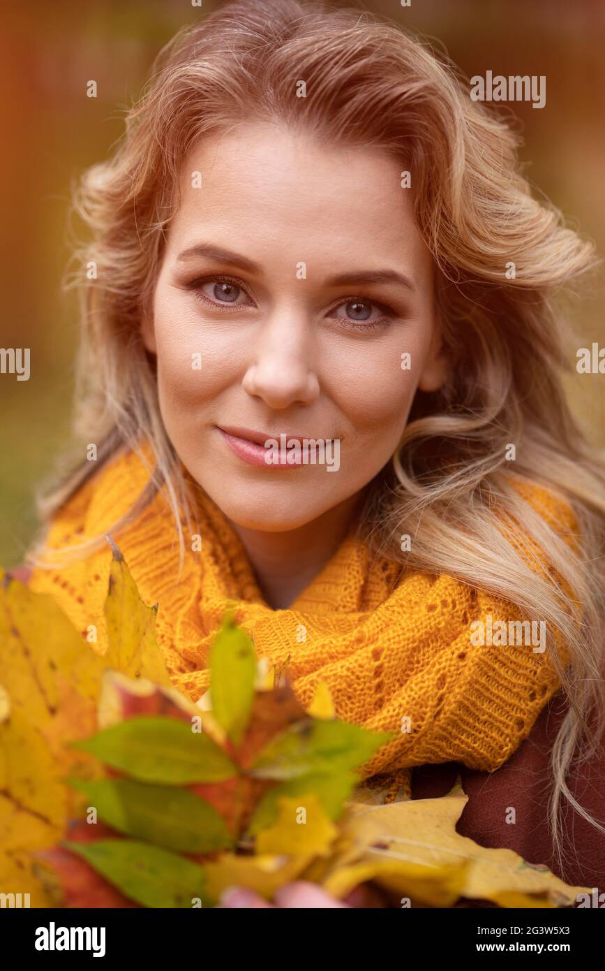 Junge charmante Frau posiert mit gefallenen vergilbten Blättern für die Kamera mit Spaziergang um Herbst gelben Garten oder Park. Wunderschönes smi Stockfoto