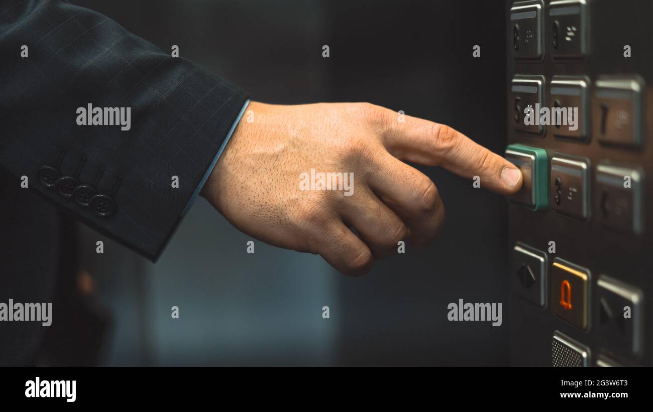 Eine Hand in einem Geschäftsanzug wird ausgestreckt, um die Bodentaste zu drücken und den Aufzug zu starten. Geschäftsmann in einem Bürozentrum elev Stockfoto