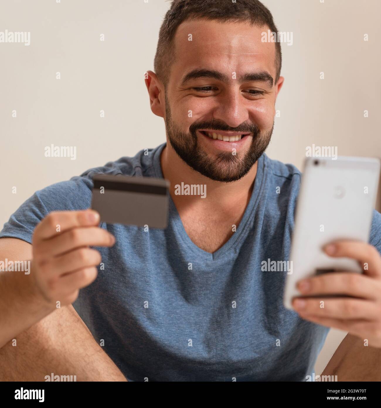 Quadratisches Bild eines fröhlichen Mannes mit Smartphone und Debit- oder Kreditkarte, der Online-Ausrüstung kauft oder Sportwetten und Glücksspiele macht Stockfoto